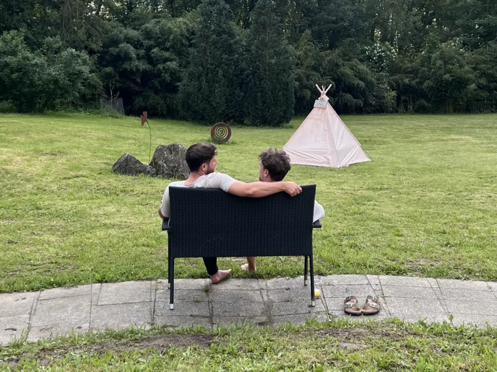 Freunde sprechen miteinander auf einer weiten Wiese mit einem Tipi Zelt im Hintergrund.
