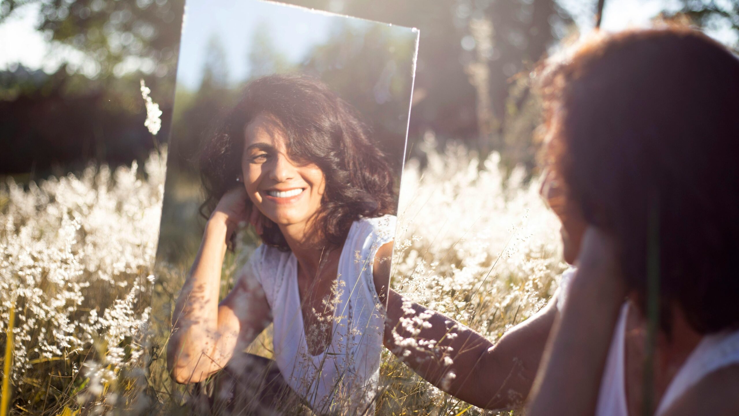 Frau praktiziert positive Selbstgespräche vor einem Spiegel auf einer Wiese.